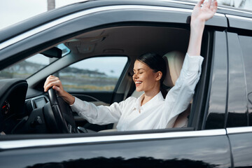 A woman sits in the driver's seat of a car with her hands raised, firmly gripping the steering...
