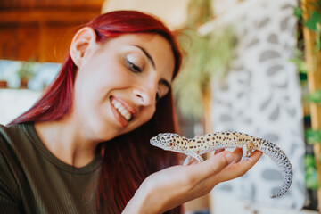 A woman with red hair smiles as she holds a leopard gecko, showing her love for reptiles. The...
