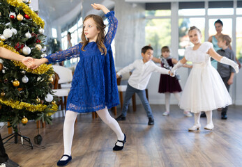 Enthusiastic tween girl in blue dress practicing partner jive moves in dance studio adorned with...