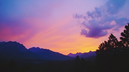 Fototapeta premium Vibrant sunset sky over serene wooded mountains with a gradient of pink, purple, and orange hues illuminating a calm natural landscape.