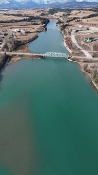 River bridge aerial vertical video overlooking distant hills with Canadian Rockies at background near Cochrane Alberta Canada.
