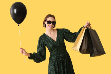 Beautiful young woman with air balloon and shopping bags on yellow background. Black Friday concept