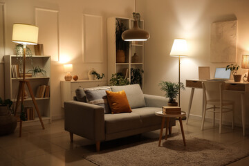 Cozy sofa, coffee table and workplace in interior of living room at evening