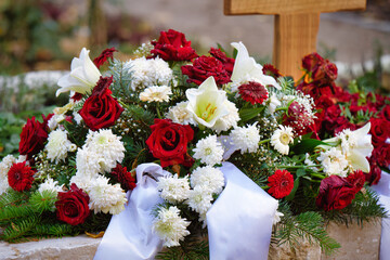 funeral flowers of red roses and white dahlias and lilies with white ribbon on a grave at a funeral