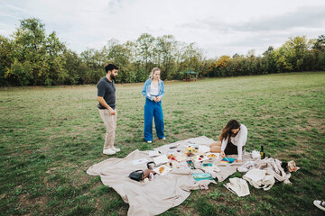 A group of friends having a relaxing picnic on a blanket in a spacious, green park. They are...