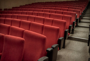 Fototapeta premium Rows of plush red theater seats in an empty cinema hall, creating a cozy and elegant atmosphere, ready for a performance or movie screening.
