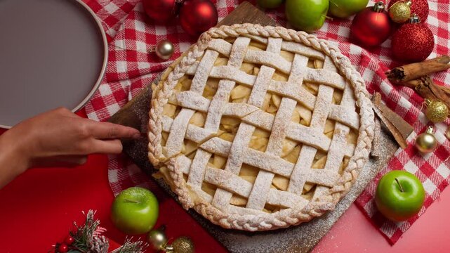 Christmas pie surrounded by a cozy decoration with Christmas details, green apples, Christmas balls, placing a slice of apple pie on a gray plate, christmas food