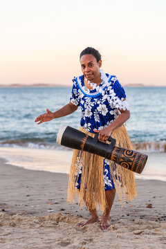 Torres Strait Islander dance performer in traditional floral dress holding drum by ocean