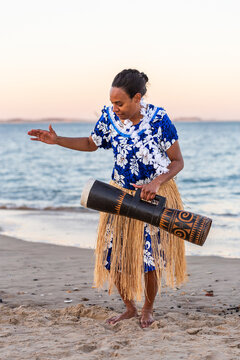 Torres Strait Island dance performer in traditional floral dress holding drum by ocean