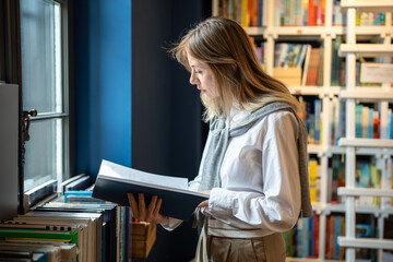Passionate woman reviews and picks books from bookshelves in bookstore or library. Female reading...