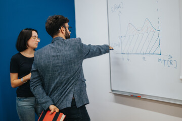 A professor explains complex data with a graph on a whiteboard to attentive students. The classroom...