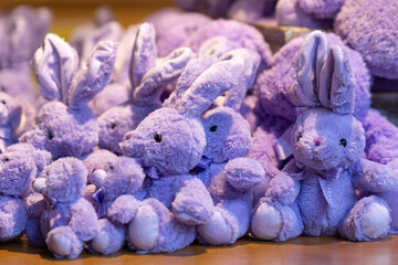 Close-up of collection of plush purple rabbits and bears neatly arranged on wooden display shelf, creating soft and cozy scene