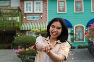 Fototapeta premium new year eve celebration concept. attractive asian young woman holding sparkler with laughing happy in outdoor garden of vintage house yard