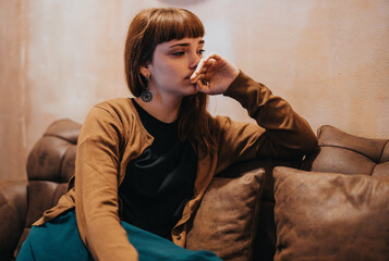 A thoughtful woman sits alone on a comfortable sofa in a cozy cafe, lost in deep contemplation. The...