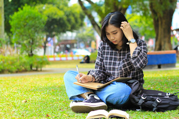 beautiful asian young woman college student focused writing on notebook and reading book in outdoors city park