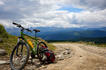 Obraz premium A picturesque scene of a green bicycle accompanied by a backpack set against the stunning mountain landscape, inspiring feelings of adventure, exploration, and the joy of cycling in nature's beauty.
