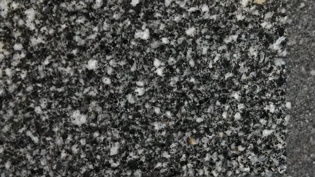 Dark textured surface with intricate patterns resembling granite in a close-up view during daylight