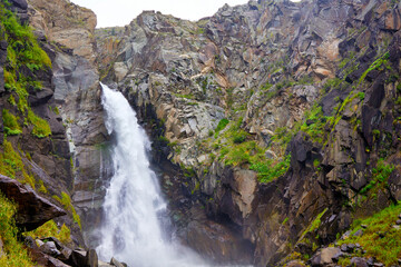 This stunning waterfall in a remote mountain area is surrounded by lush greenery and towering rocks, creating a refreshing atmosphere perfect for relaxation and reflection.
