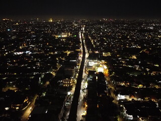 Aerial night view of a long, illuminated road cutting through a densely populated city.