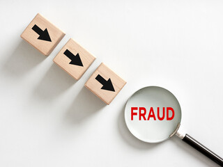 Magnifying glass showing fraud word and wooden cubes with arrows pointing towards it