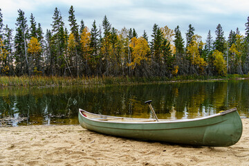 A green canoe sits on the beach next to a body of water