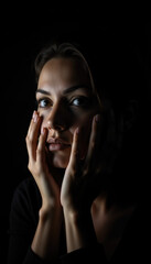 Fototapeta premium Expressive Portrait of a Young Woman with Hands Framing Her Face, Captured in Dramatic Low-Key Lighting and Deep Shadows
