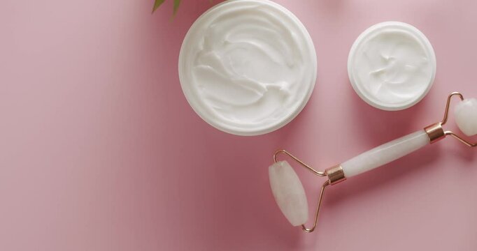 Top view White bottle, serum, facial pink roller with palm leaf rotate for cosmetics on pink background in studio. Cosmetics oil based on natural ingredients, scrub, tonic, body care. Top view.