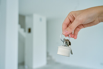 Close up hand holding keys with house shaped keychain in front of blurred new apartment interior....