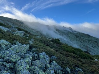 Rocky mountain slope covered in mist with a vibrant blue sky and scattered vegetation