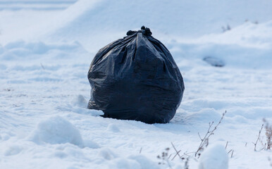 A black trash bag is sitting in the snow