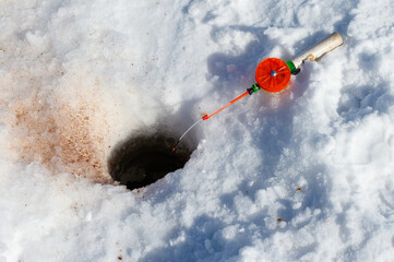 A fishing pole with a green and orange lure is in the snow