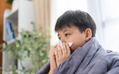 Young asian boy sneezing or blowing his nose and mouth with tissue, cold allergies or illness,...