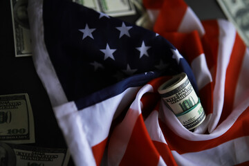 American Flag and Rolled US Dollar Bills Surrounded by Scattered Money Signifying Economy and...