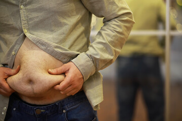 Man Holding Belly Fat in Front of Mirror to Show Weight Gain