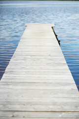 Fototapeta premium Wooden Pier Extending into Calm Lake Waters with Clear Blue Sky Reflections