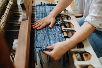 Close up of woman working on wooden loom, weaving a rug from old fabrics. Upcycling in business and...