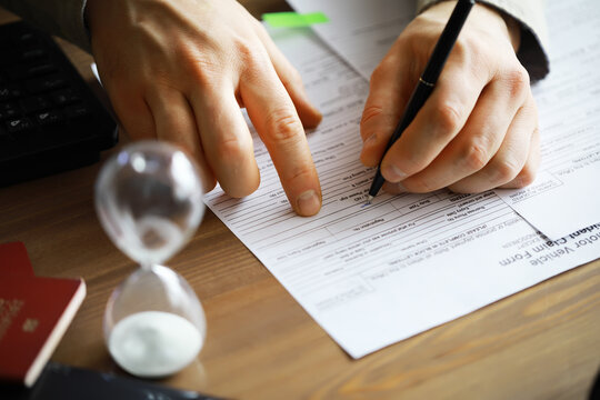 Businessman Filling Out Forms with Pen and Hourglass on Wooden Desk