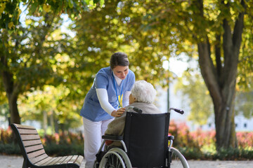 Disabled elderly woman in wheelchair talking with her nurse, sharing her problems with female...