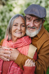 Portrait of beautiful senior couple outdoors in an autumn garden. Elderly husband and wife are...