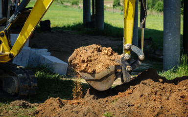 Mini excavator digs a narrow trench in soil for laying communications close-up. Mini bucket of...