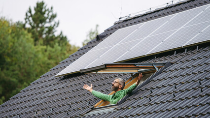 Man looking from skylight, roof window with solar panels above him. Sustainable lifestyle and green...