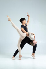 One Sportive Couple of Asian Man and Caucasian Woman Performing As Ballet Dancers Over Grey in Studio During Suppots in Classical Dance © danmorgan12