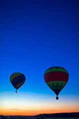 Fototapeta premium Two Amazing Colorful Air Balloons Levitating Over the Ground Outdoors Against Clear Blue Sky