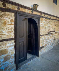 A pair of dark wooden doors stand open against a backdrop of stone walls and a charming lantern.