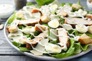 Delicious Caesar salad with chicken on grey wooden table, closeup