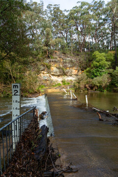 Water over causeway on remote road with depth indicator.