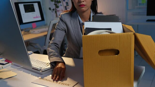 Businesswoman holding resignation letter in box with personal belongings at desk in office for changing job. Concept of resignation or changing job for future.