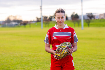 Portrait of female Aboriginal teenager holding AFL footy ball on sports ground field