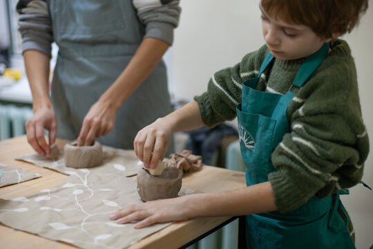 Close up of little boy sculpting cup from clay. Children's workshop at pottery studio. Creating ceramics with own hands. Selective focus.