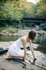 Fototapeta premium A tranquil young woman sitting calmly by the river while wearing a lovely summer dress